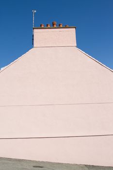 A pastel pink gable end with a chimney and pots against a blue sky.