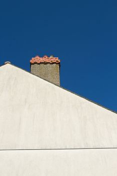 A pale coloured gable end with a chimney with ornate red brick against a blue sky.