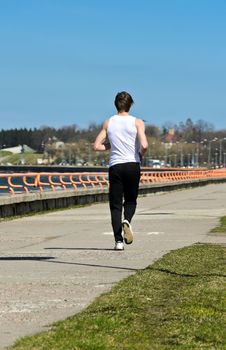 Athletic young male running on the shoreline. From the back