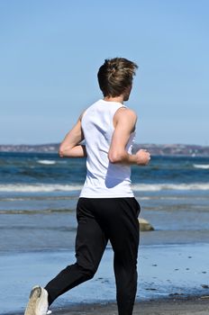Athletic young male running on the beach. From the back