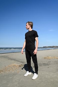 Young male in black clothes and white shoes standing on the beach