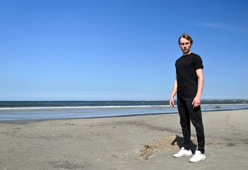 Young male in black clothes and white shoes standing on the beach