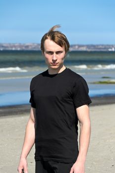 Young male in black clothes and white shoes standing on the beach