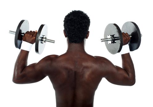 Rear view of a young male bodybuilder doing heavy weight exercise with dumbbells