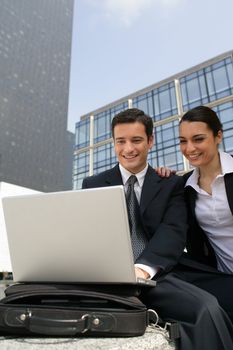 Businessman and businesswoman laughing in front of a laptop outdoors