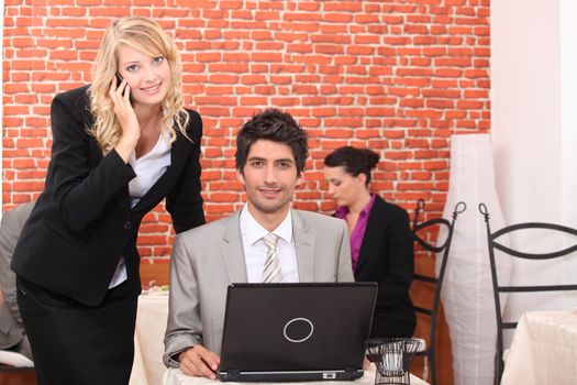 Business couple in a restaurant using a laptop and telephone