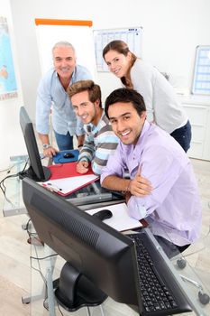 Four smiling people gathered round a computer in a classroom