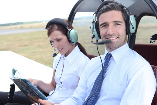 Smiling man sitting in the cockpit of a light aircraft as his partner consults a mapbook