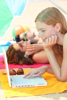 Three female teenagers with a laptop on the beach