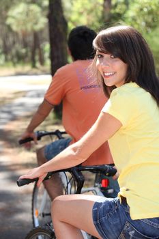 Pretty young woman and her boyfriend riding bikes through the woods