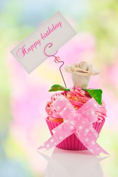 A beautiful pink happy birthday cupcake with flower and a label for your text as studio shot