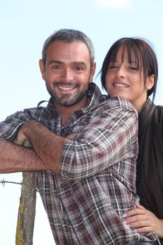 Farmer and wife stood outdoors by fence