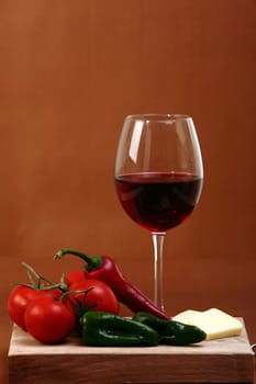 Red wine on brown background with cheese and vegetables