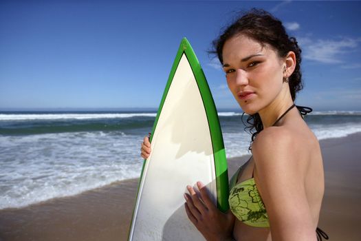 Brunette stood on beach with surfboard