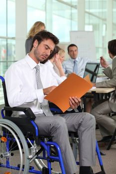 A group of business people in a meeting room, one of them in a wheelchair.