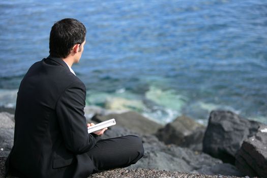 Businessman sat on rock by the sea