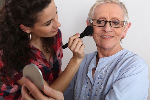 Young woman applying blush on her grandmother's cheeks