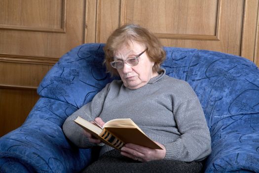 The old woman sits in an armchair and reads the book