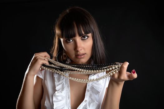 The thoughtful girl with pearl beads in hand on a black background