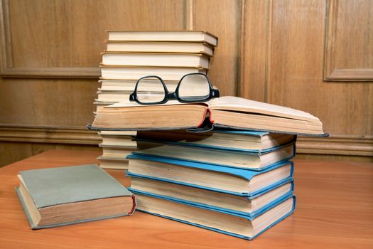 Pile of books and old glasses on a table in study