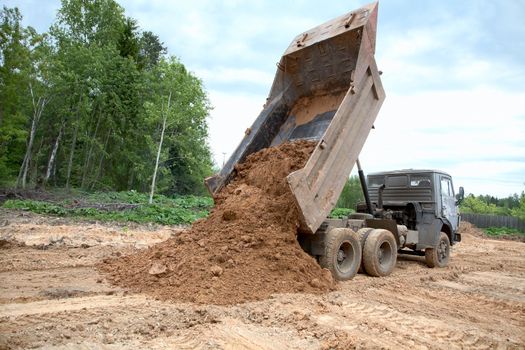 dump-body truck unloads a ground on the land