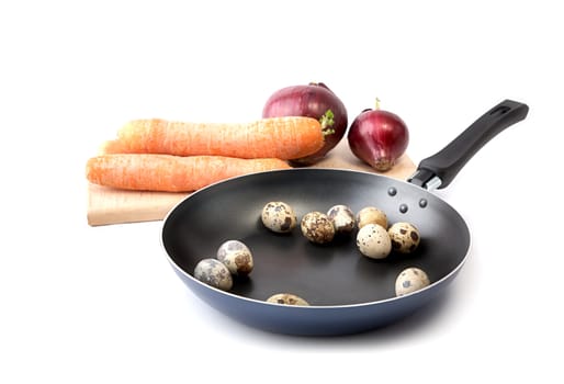 Carrots, onions on a chopping board and quail eggs on  frying pan
