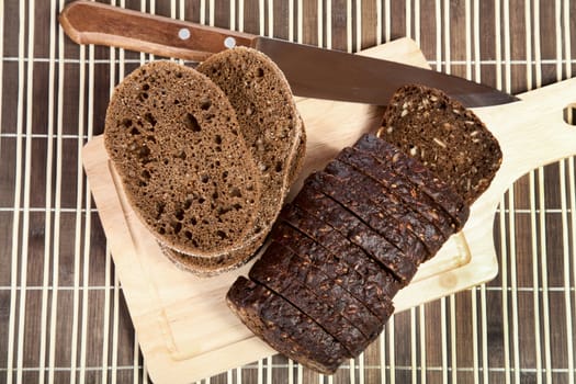Slices cut black bread with  knife on a chopping board
