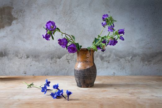 Still-life with fading flowesr  in a jug against rough wall