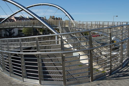 The steel structure of a bridge with ramp and stair access and metal railings with a blue sky in the background.