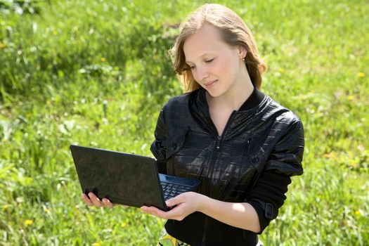 girl-teenager with the laptop against a green grass in the sunny day