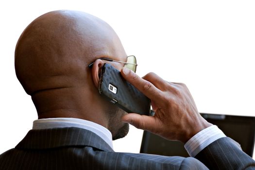 A business man in his early 30s talking on his smart phone and working on his laptop or netbook computer.