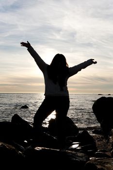 Silhouette of a young woman posing on the beach with her arms up in the air.