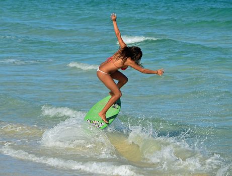 sensuous young woman surfer skim boarding in the surf on miami beach