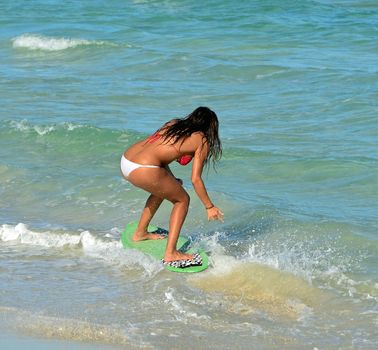 sexy woman surfer wearing a white bikini bottom and a red bikini top riding on a skimboard