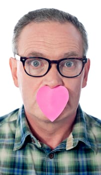 Surprised aged male with paper heart over his mouth. Eye wide open. Love concept