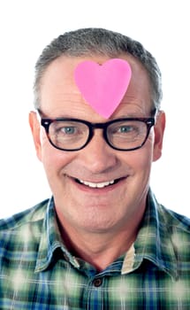 Handsome senior man with paper heart on his forehead. Smiling at camera, closeup shot