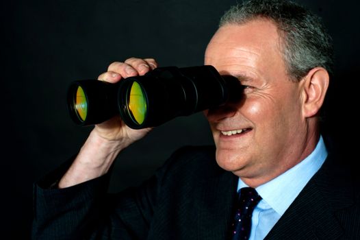 Aged executive monitoring through binoculars isolated over black background