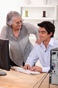 Young man using computer and happy senior woman