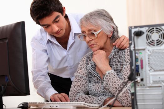 Young man showing elderly lady how to use computer