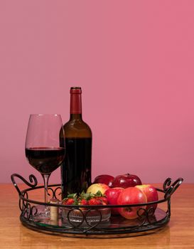 Red wine bottle and red wine in glass with red apples, grapes and strawberries