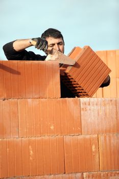 bricklayer in construction site erecting red brick wall