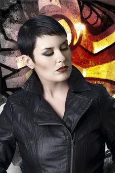 Sexy brunette young woman in a leather jacket over graffiti background with intense orange light