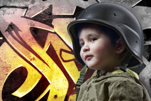 Baby playing war with military helmet against graffiti background with intense orange light