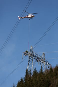 Working with new high-voltage power line that is stretched. The work takes place in one of the masts with helicopter.