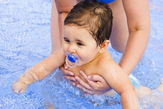 Newborn baby with a pacifier playing in the pool with his mother