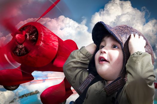 An adorable baby boy over a red planeputting his hands to his head wearing an old-fashioned pilot's