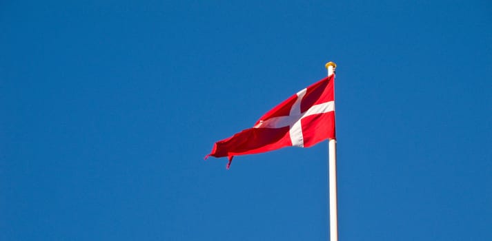 Danish flag in the wind, dannebrog, against blue sky