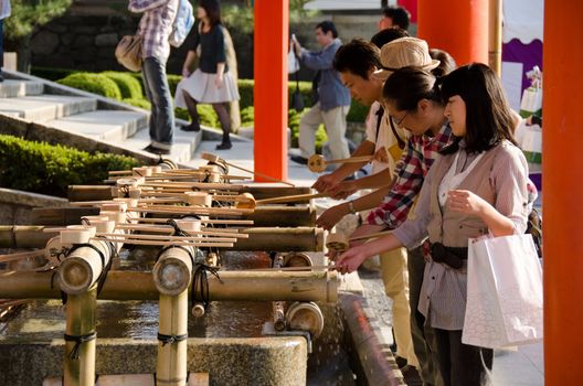 People washing hands at a Tsukubai in front of the Inari Shrine in Kyoto in order to purify themselves by the ritual washing