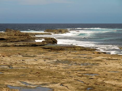 Tidal rock platform in australia with ocean in the background and neutral sky