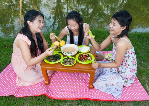 Asian Thai girls picnic together beside swamp.